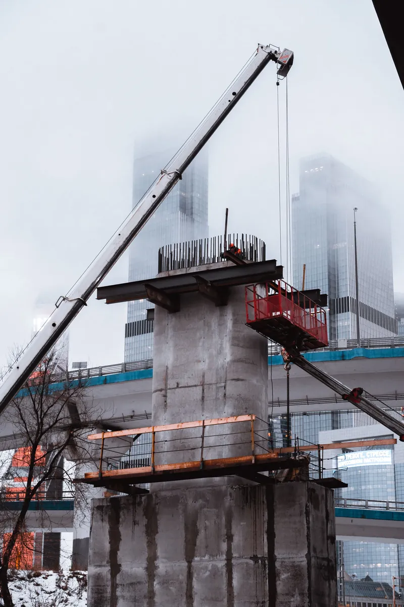 Baustelle im Nebel: ein Kran setzt einen Stahlträger auf eine frisch betonierte Stütze