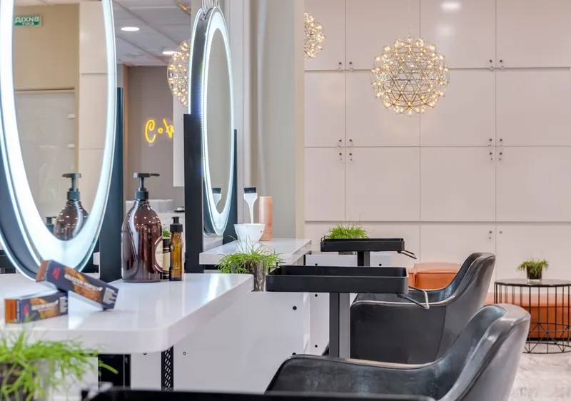 Blick in den Salon: eine Reihe von Arbeitsplätzen mit runden, beleuchteten Spiegeln und dunklen Ledersesseln